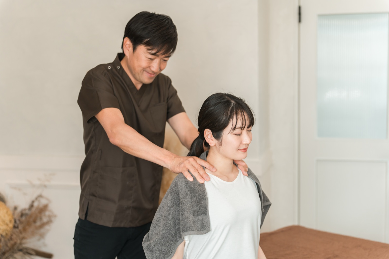 施術着のスタッフが女性の両肩に手を当てて確認する様子