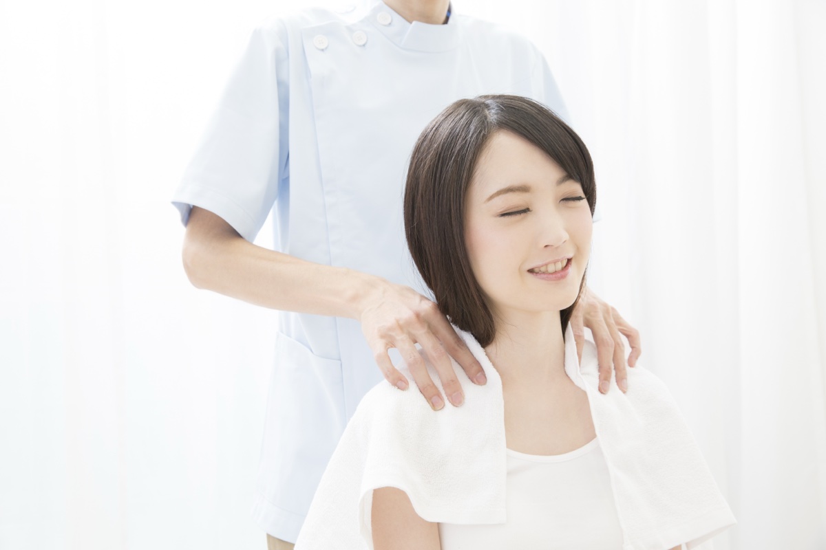 椅子に座りタオルを肩にかけた女性の両肩に手を置く施術者