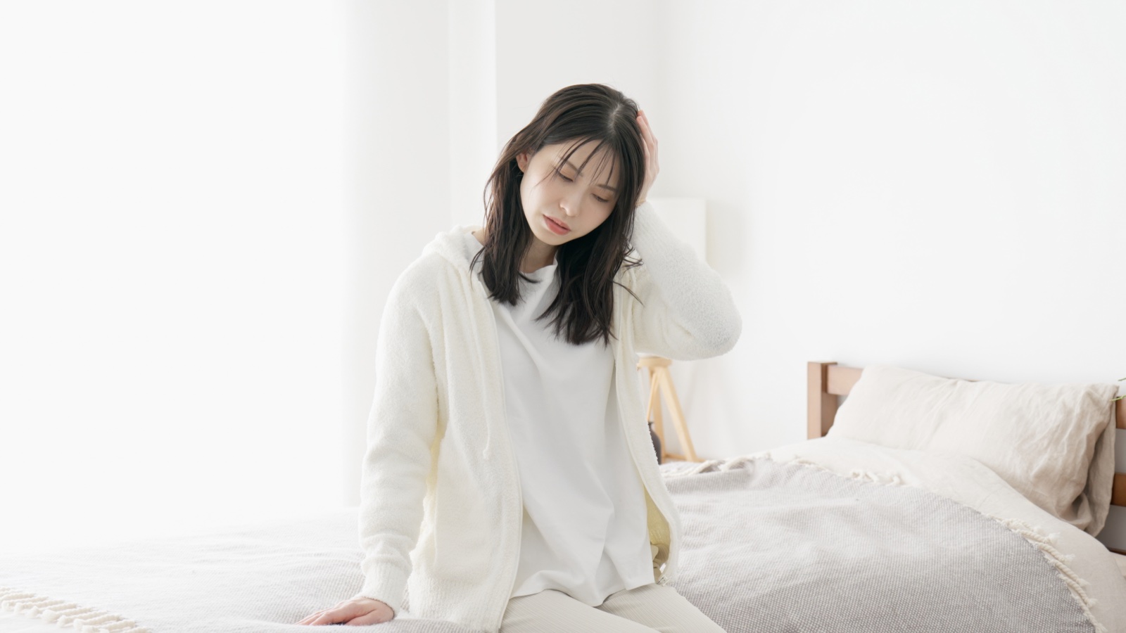 ベッドの端に腰かけ片手を頭に当ててうつむく女性