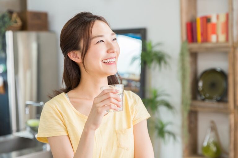 キッチンの前でグラスの水を持ってほほえむ女性