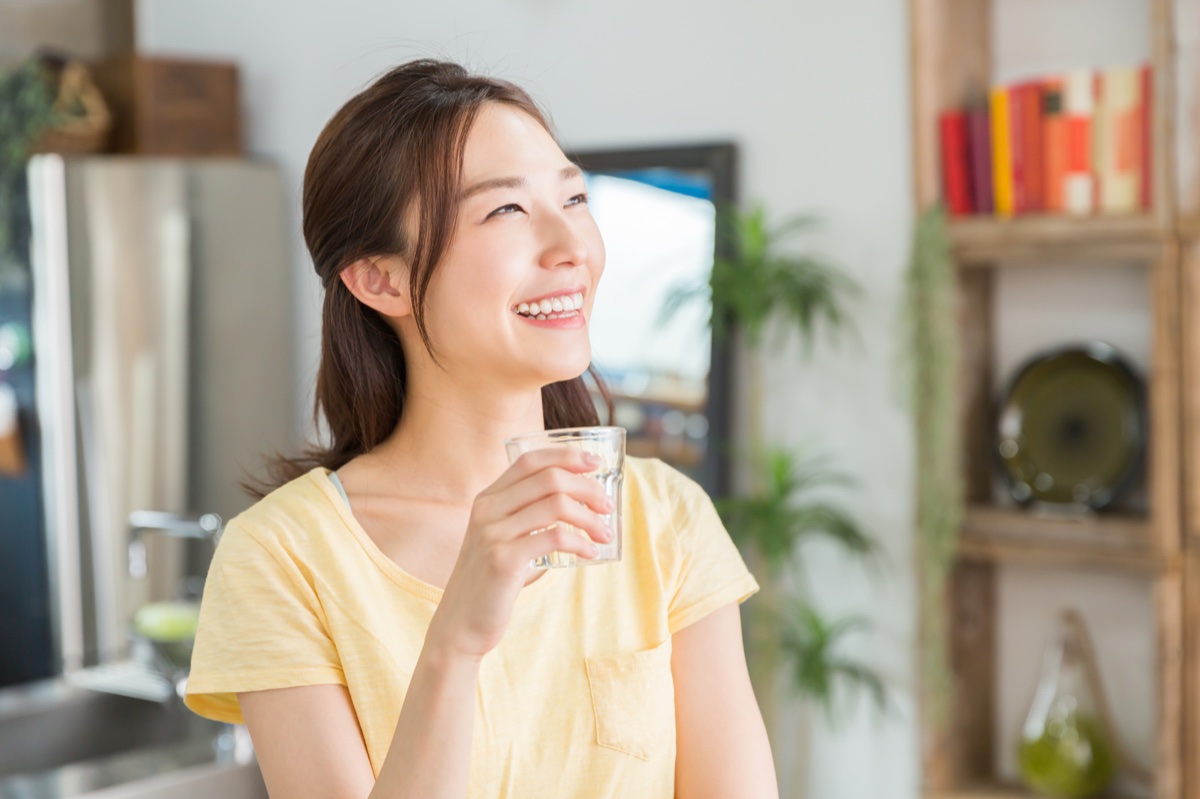 キッチンの前でグラスの水を持ってほほえむ女性