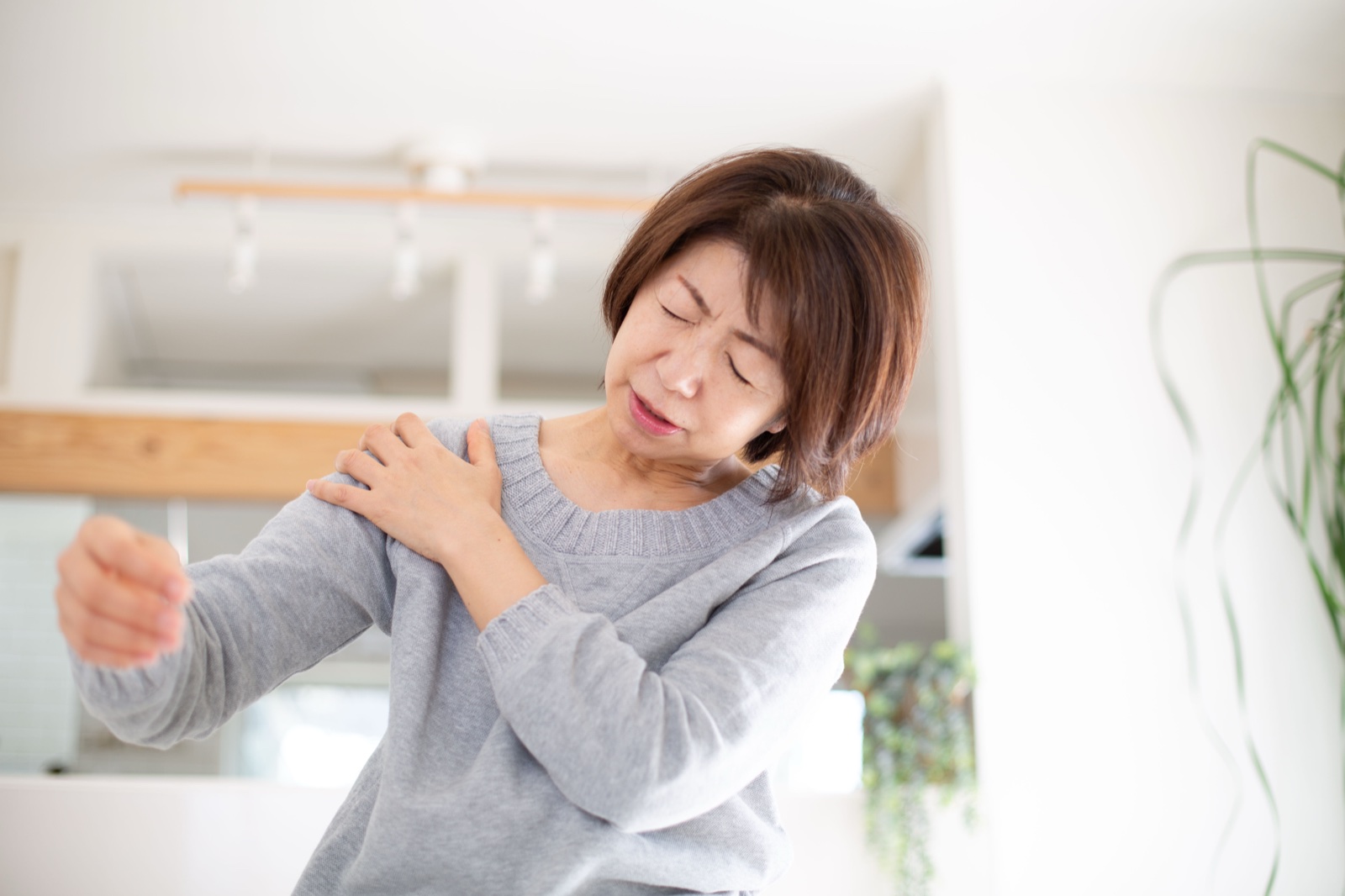 腕を前に伸ばしながら肩を押さえて顔をしかめる女性