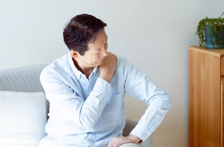 ソファに座り片手で反対側の肩を押さえる男性