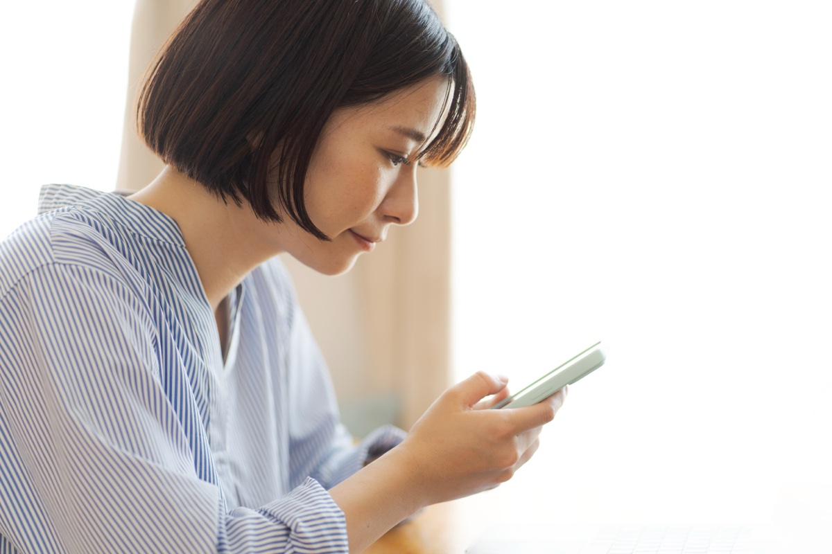 うつむいてスマートフォンの画面を見る女性