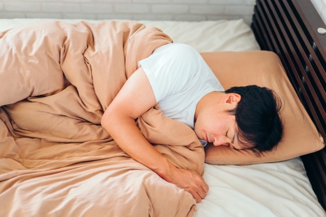 掛け布団を抱えて体を半分うつ伏せにして眠る男性