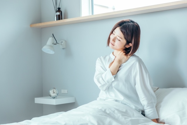 ベッドで上体を起こし首の後ろに手を当てる女性