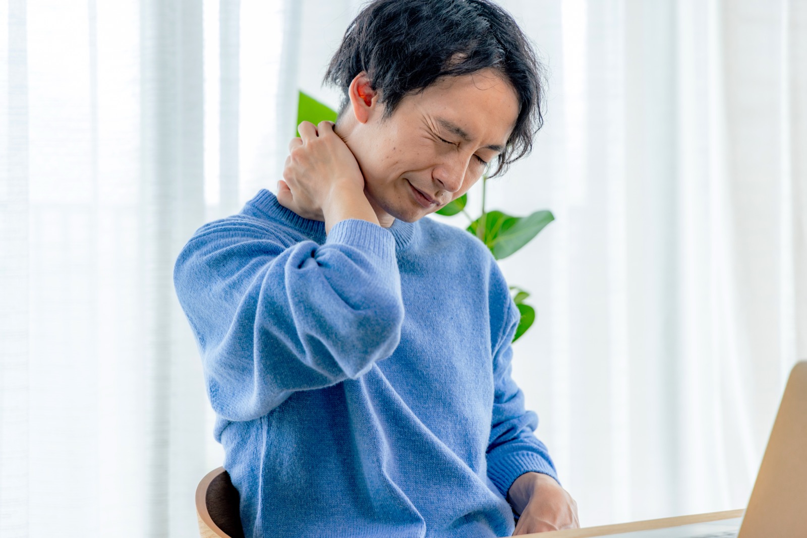 首の後ろを押さえて顔をしかめる男性