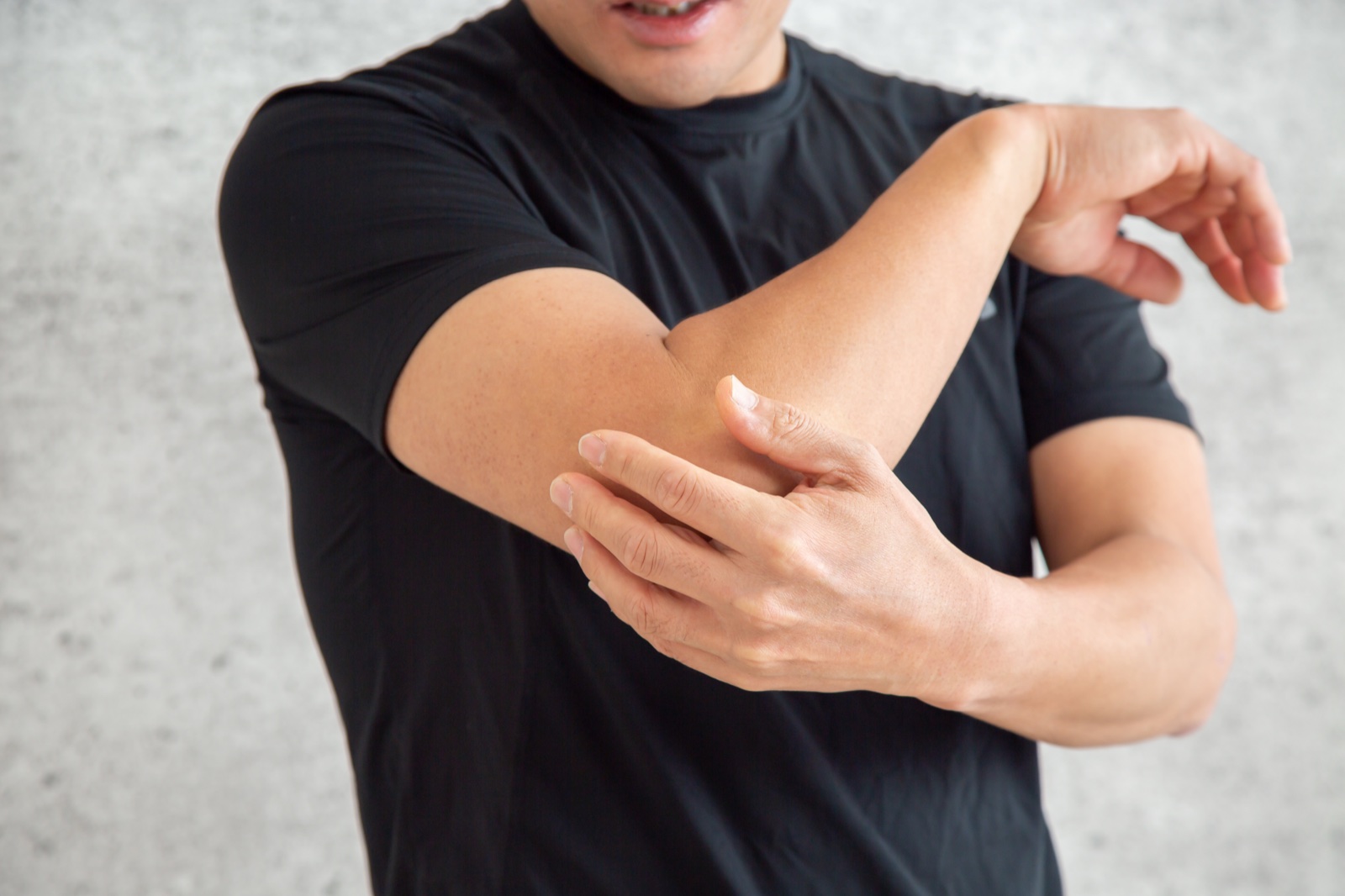 黒いTシャツの男性が曲げた腕の肘を片手で押さえる