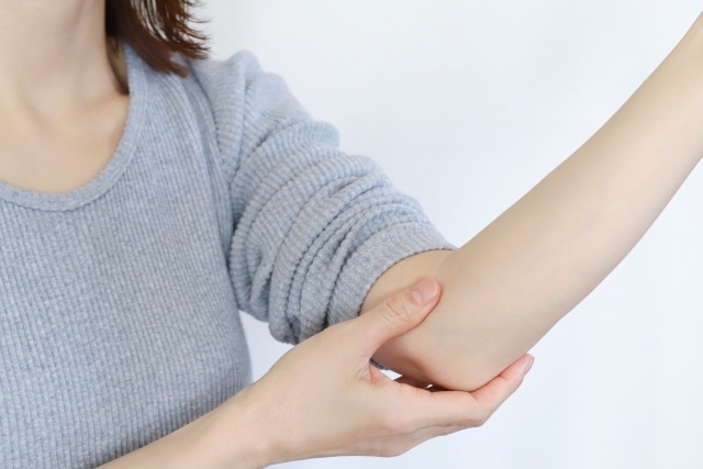 グレーのニットの女性が片手で反対の腕の肘を支える