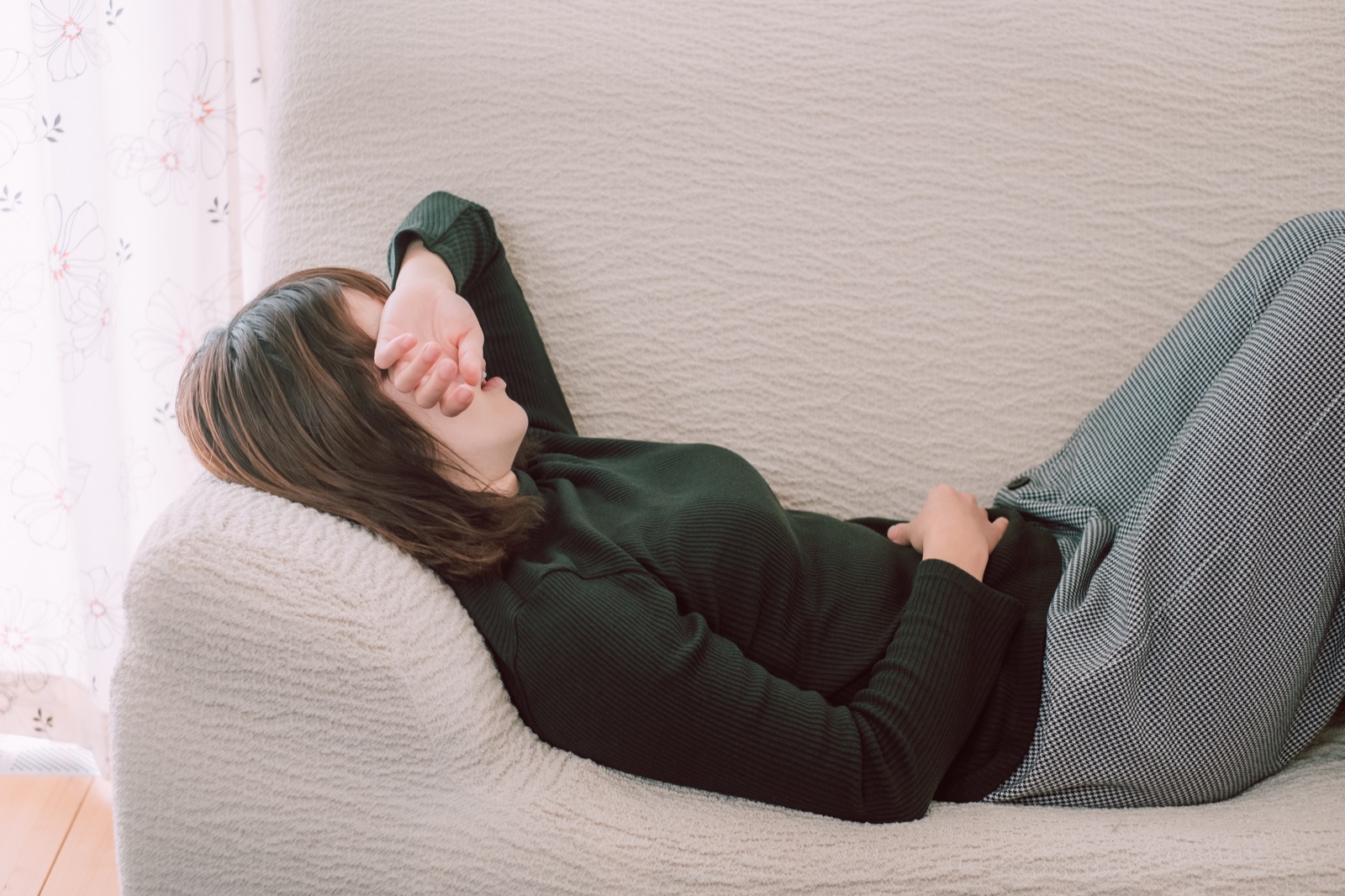 ソファにもたれて片腕で目元を覆い横になる女性