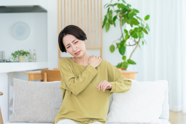 ソファに座り顔をしかめて片手で肩を押さえる女性