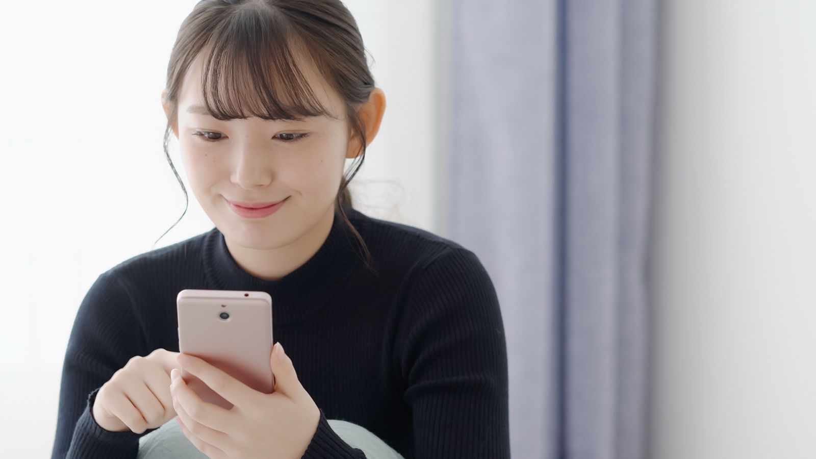 黒いニットの女性がスマートフォンを見ながら画面を操作する