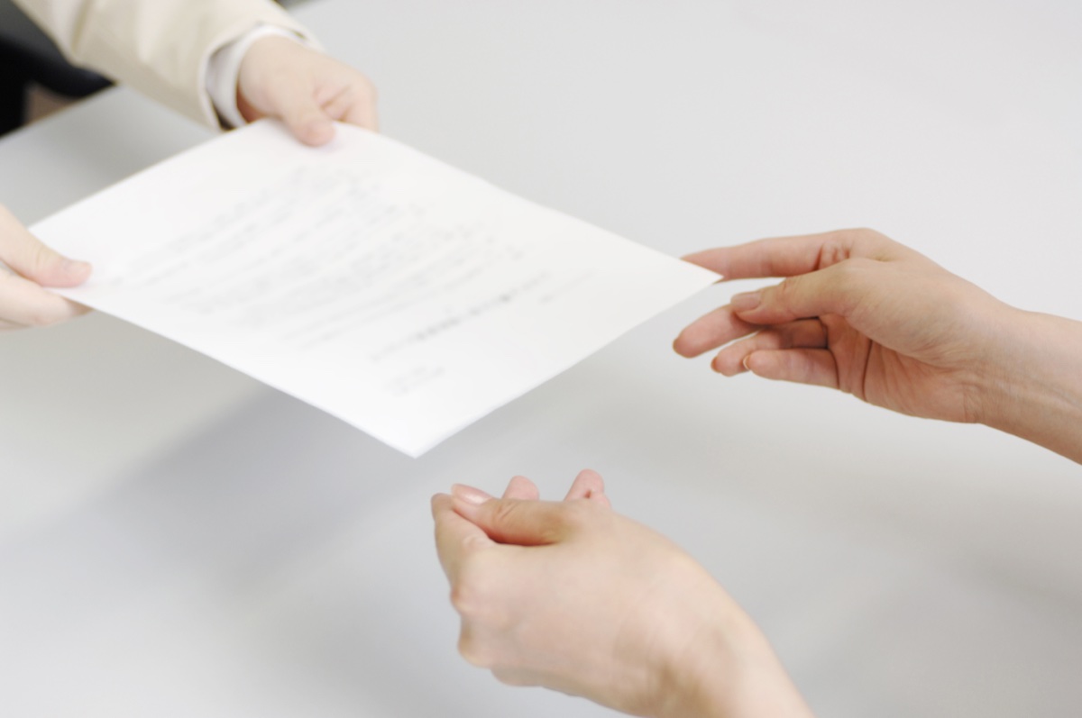 明るい机の上で、白い書類を差し出して手渡す二人の手元