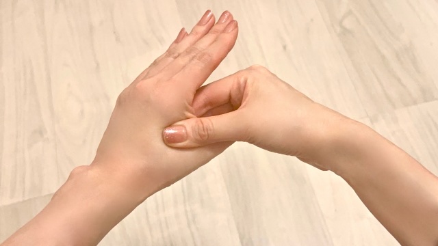 木目の床の上で、親指と人差し指の間を反対の手の親指で押す